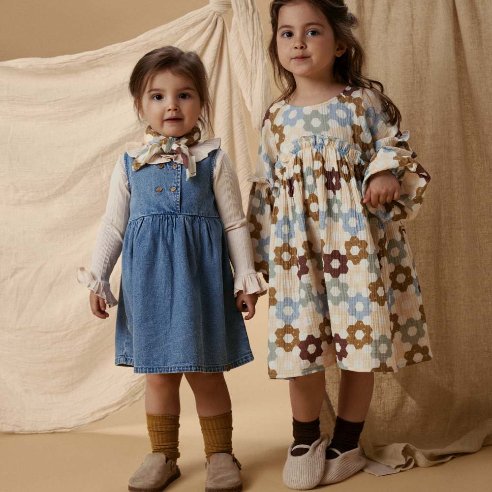 Two girls in dresses stood side by side in front of a hung sheet 