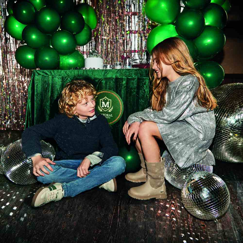Two children sat on the floor among disco balls and green balloons 