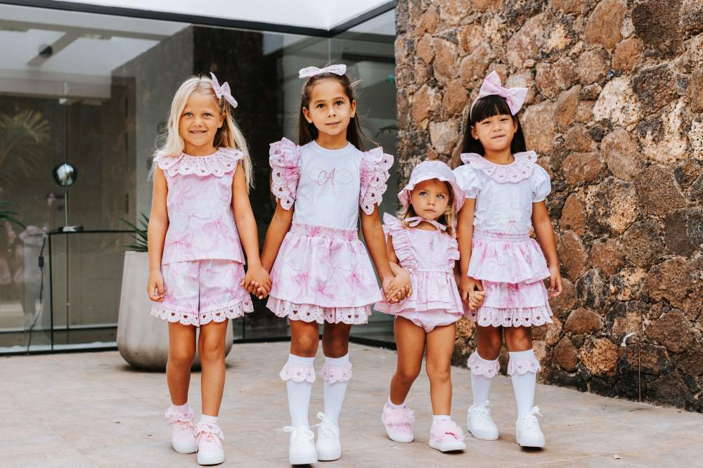 Four girls in pretty outfits by Picture Book Fashion holding hands outside a building