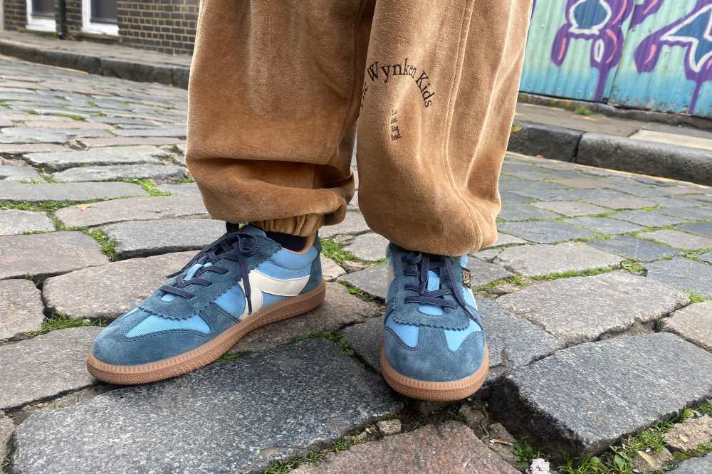 A child's feet in blue Young Soles sneakers shown stood on a cobbled street 