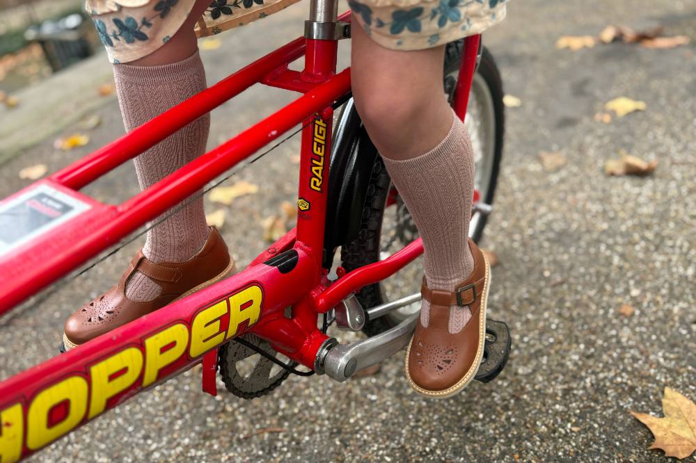 A child wearing brown Mary Jane shoes by Young Soles riding a red Chopper bike 