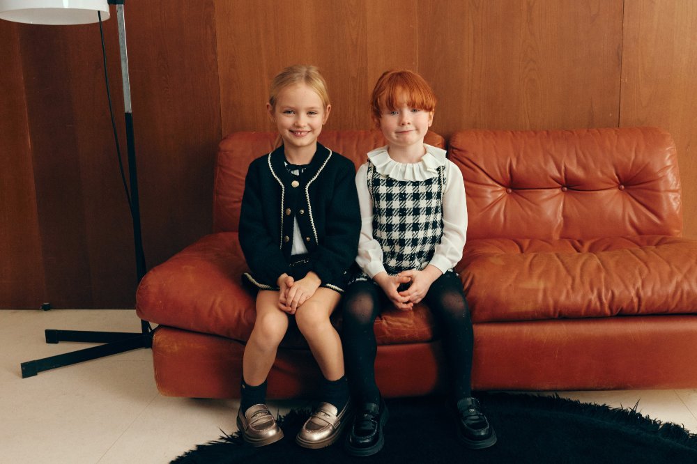 Two children in black and white outfits sat in a room on an orange leather sofa