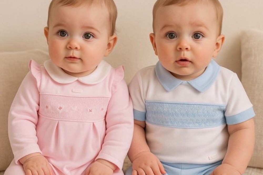 Two babies sat wearing pink and blue outfits by AMORE