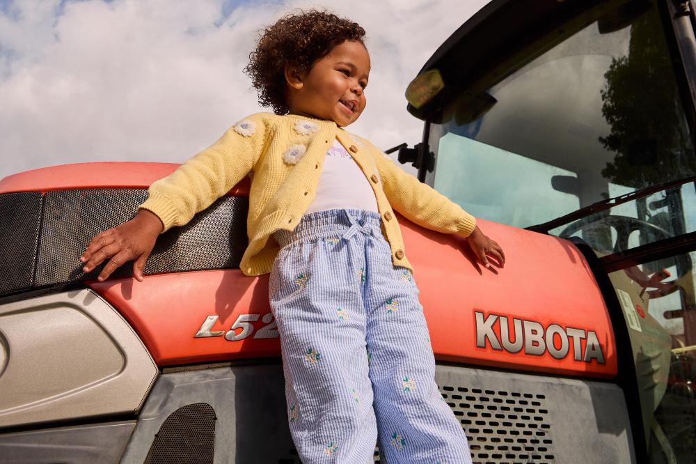 A young child stood on a tractor wheel promoting the new JoJo Maman Bebe x Godstone Farm campaign