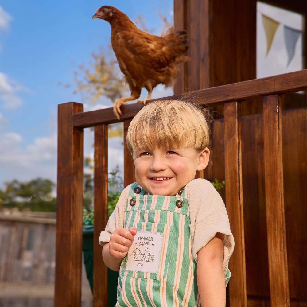 A young boy outside at Godstone Farm next to a chicken promoting the new Jojo Maman Bebe collection