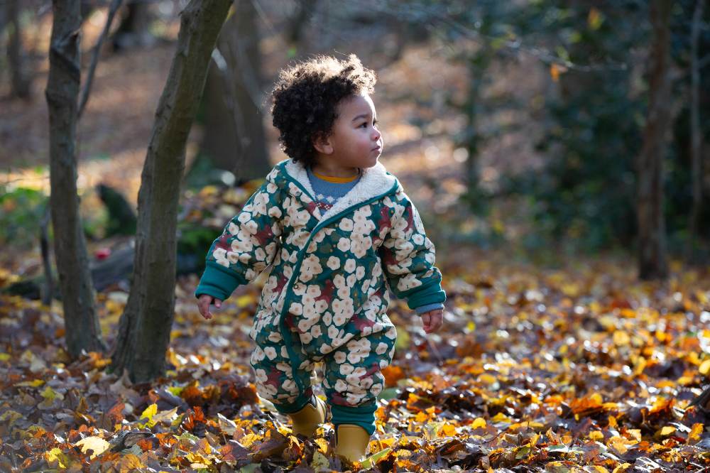 A young child in a wood wearing a patterned snowsuit by Little Green Radicals 