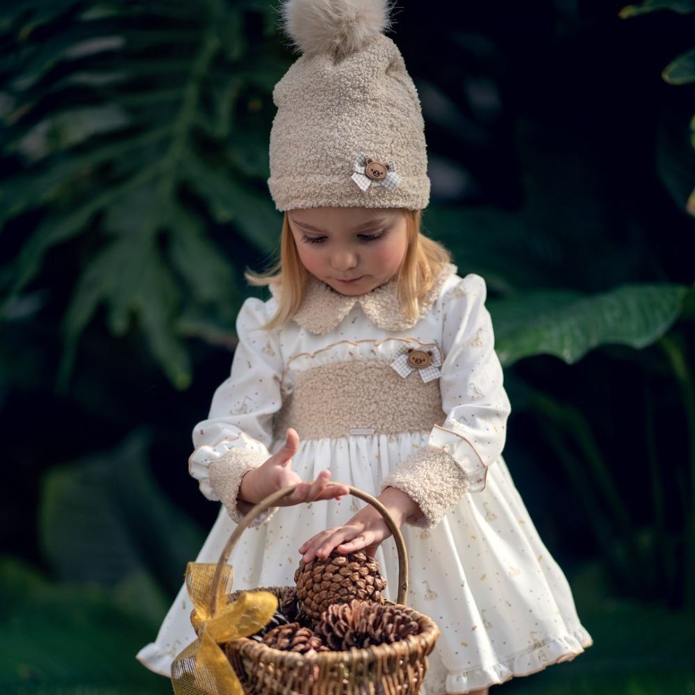 A girl outside wearing a bobble hat and dress and holding a basket of pine cones 