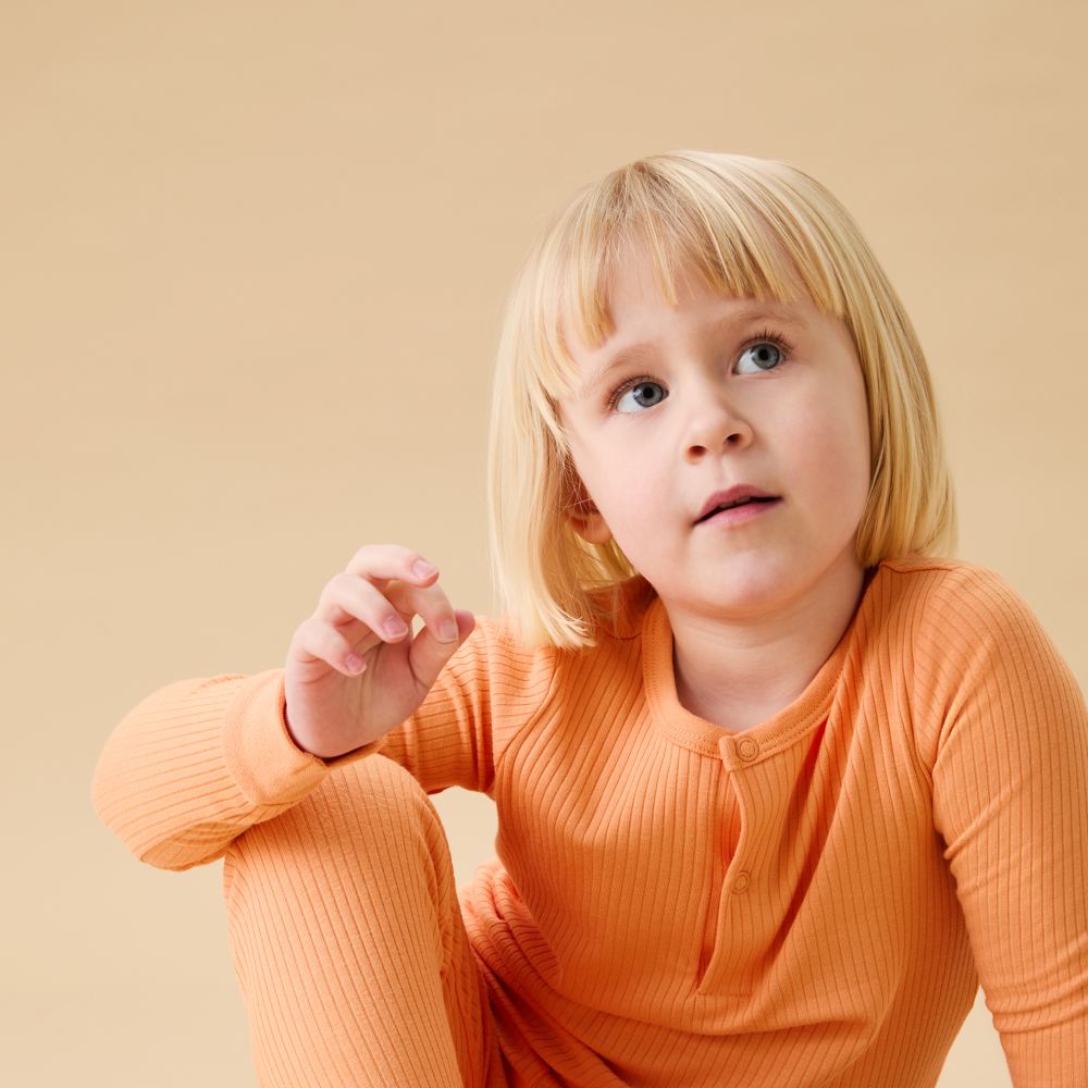 A young girl sat in orange pyjamas by MORI