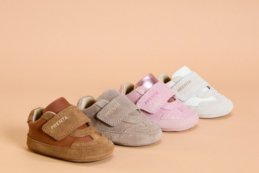 Four children's shoes by PRENTA displayed in a row on a pink background