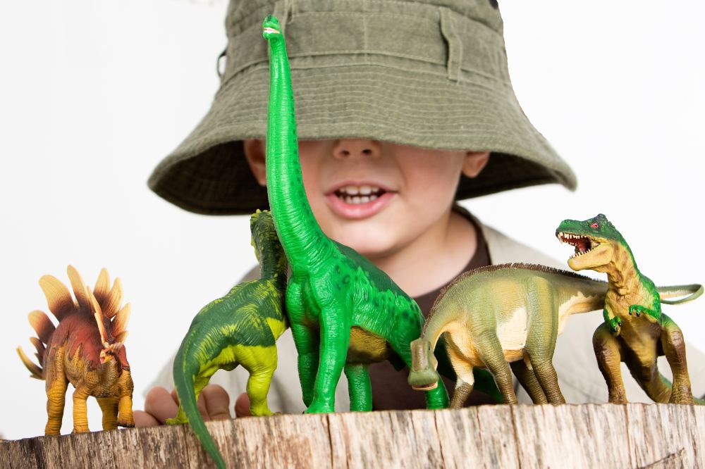 A child with a hat pulled over his face behind a set of toy dinosaurs