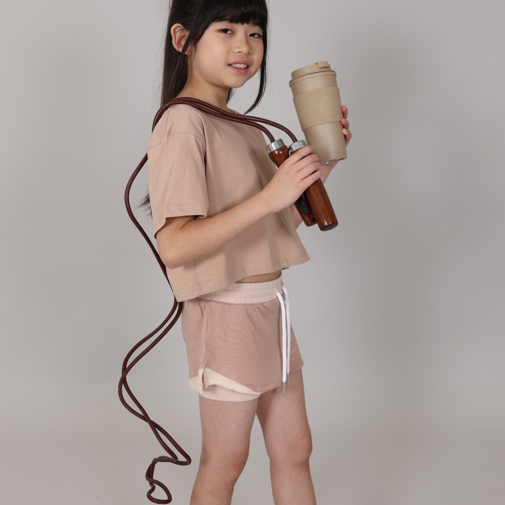 A girl holding a skipping rope and cup wearing a beige T-shirt and shorts by Svante 