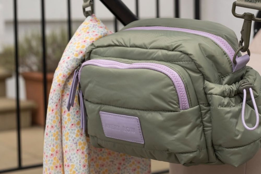 An Avery Row pram organiser hung on the back of a pram with a floral print muslin cloth available on the JoJo Maman Bébé website