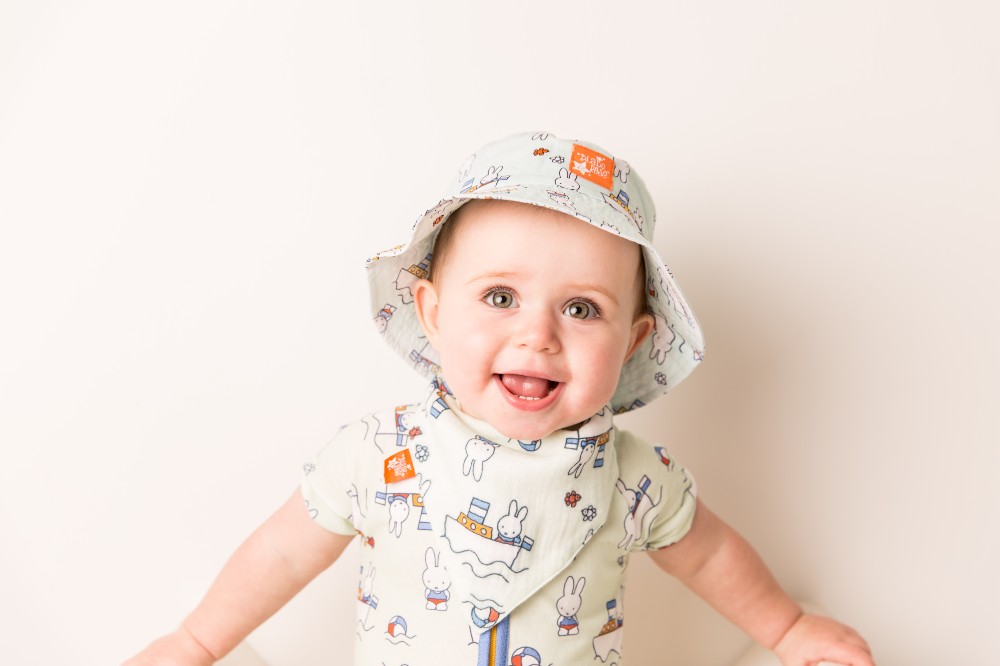 A baby in a Miffy print summer babygro and sun hat by Blade & Rose