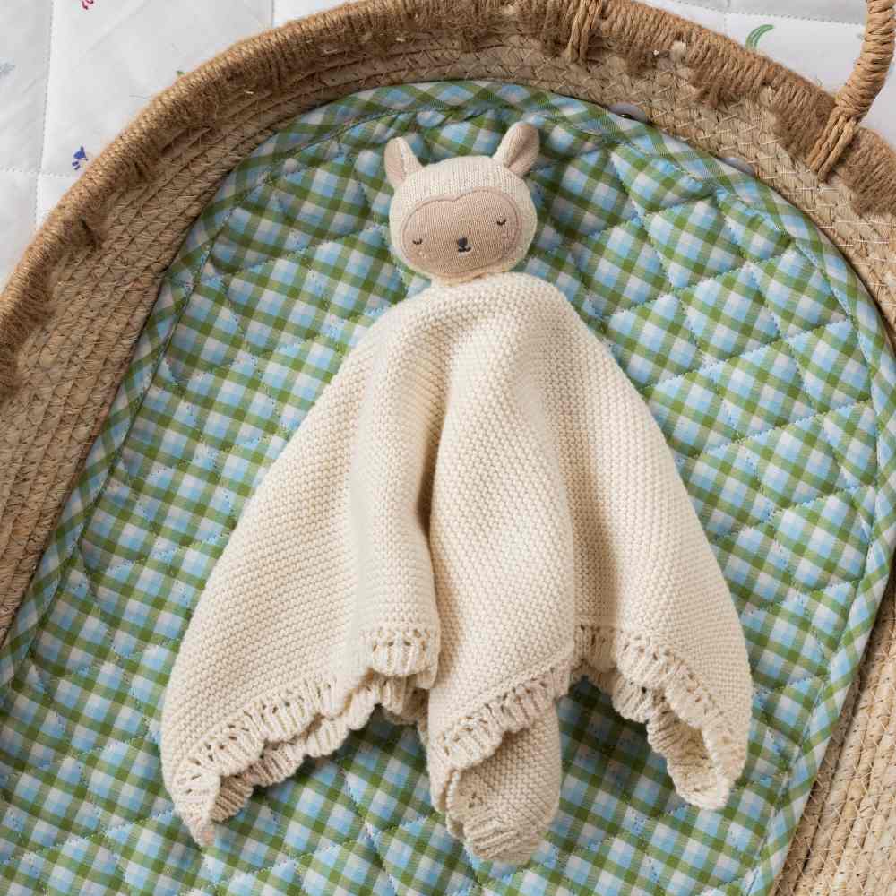 A child's knitted comforter toy from Avery Row's Farm Collection displayed in a baby basket 