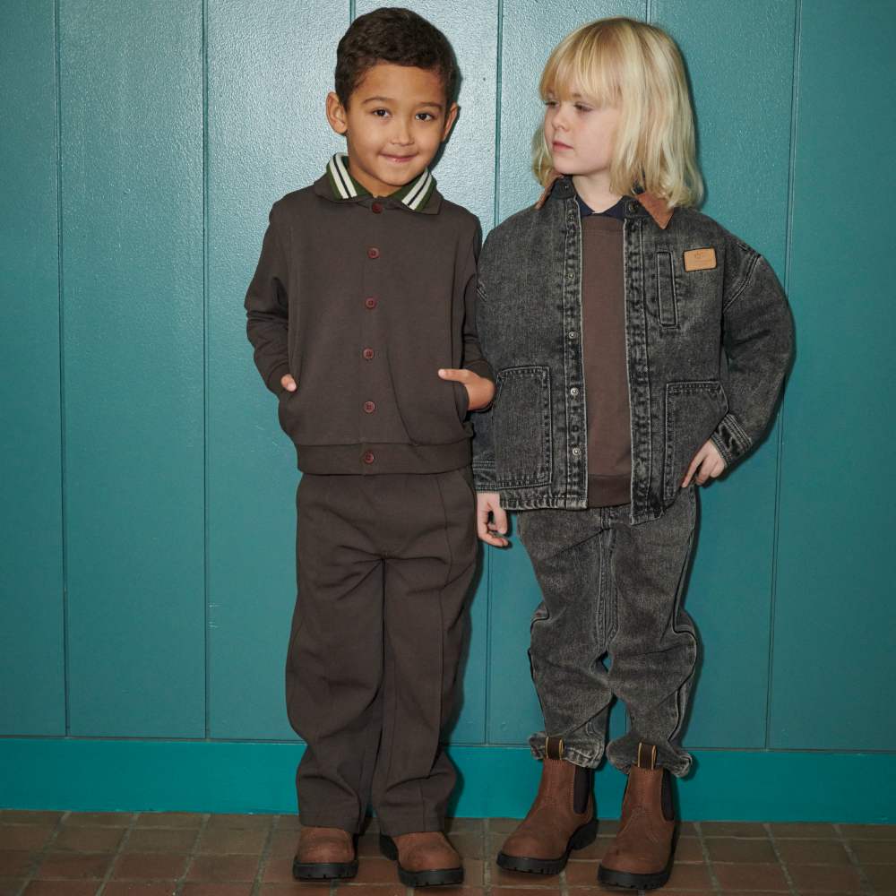 Two children in winter outfits stood in front of a blue panelled wall 