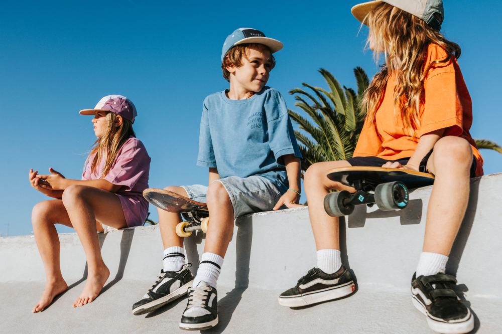 Three children sat on a wall outside in the sun wearing outfits by Roarsome
