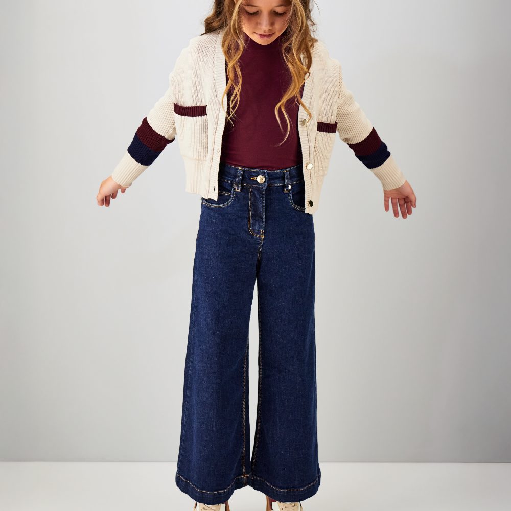 A girl stood on her tip toes looking down wearing a cardigan and wide leg jeans 