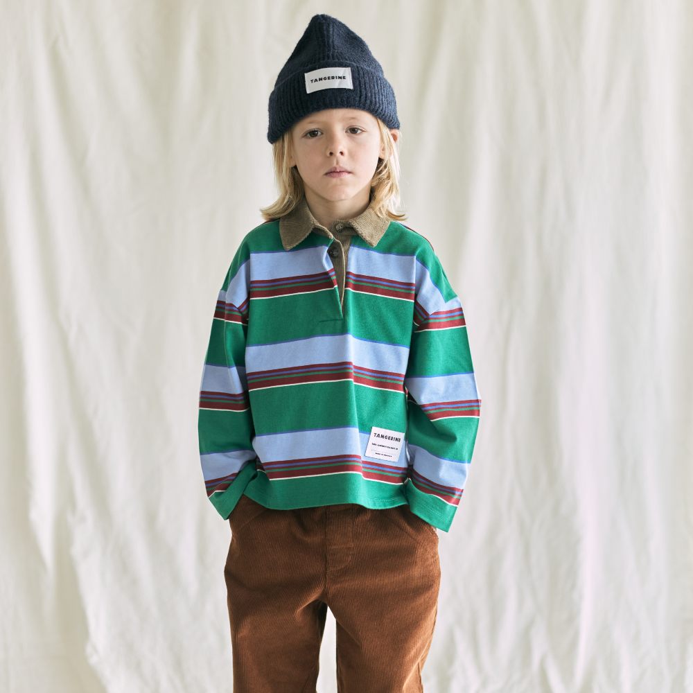 A boy stood against a white background wearing a hat, striped top and trousers 