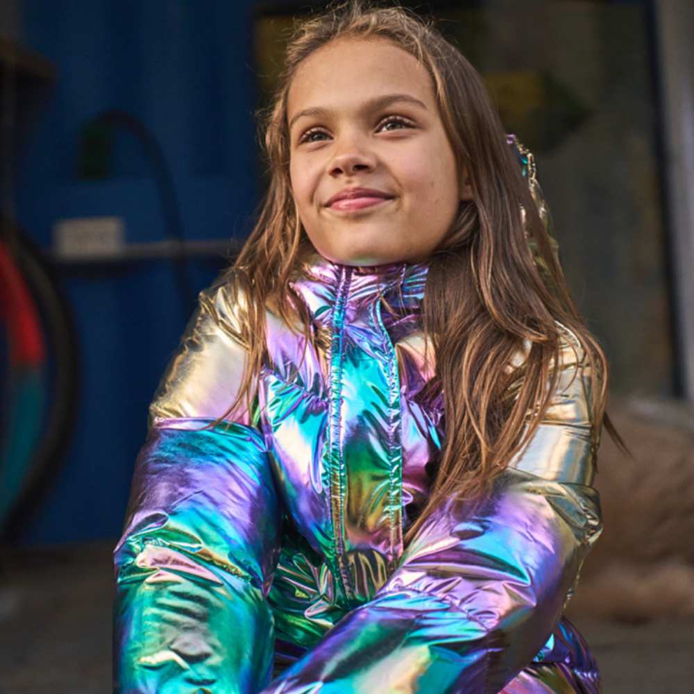 A girl sat down wearing a colourful metallic coat 