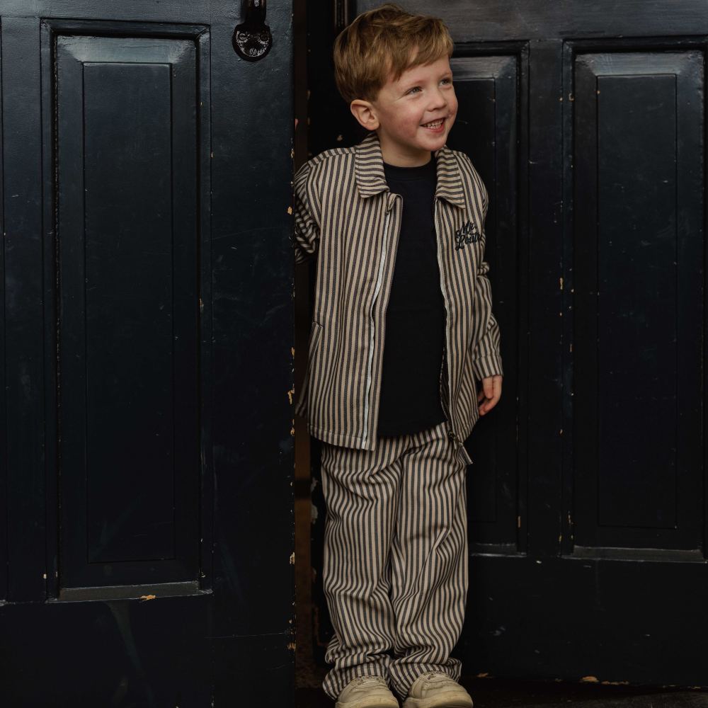 A boy stood in a doorway wearing a striped shirt and matching trousers 