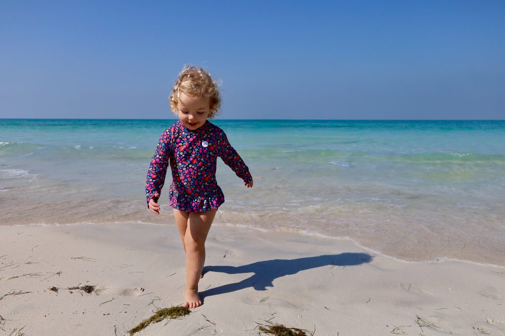 A young girl in a long sleeve swimsuit running on a beach