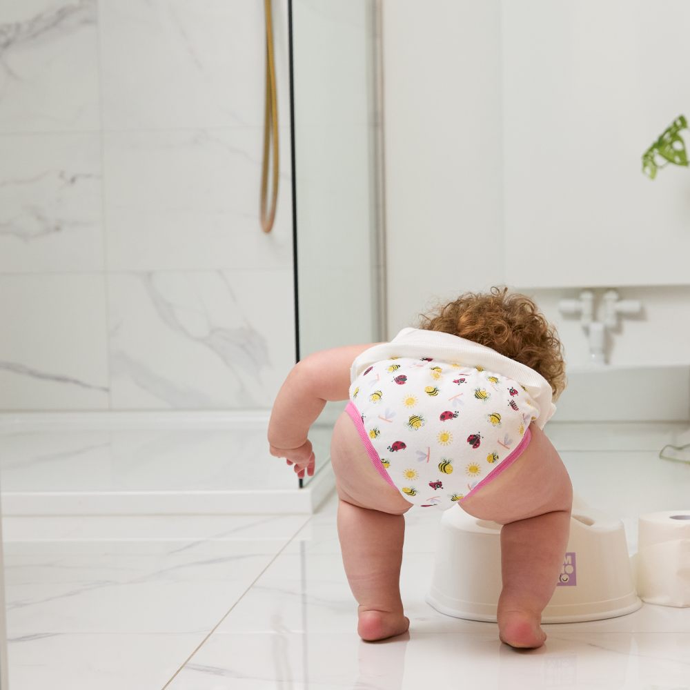 A babywearing a printed nappy by Bambino Mio bending down to the floor 