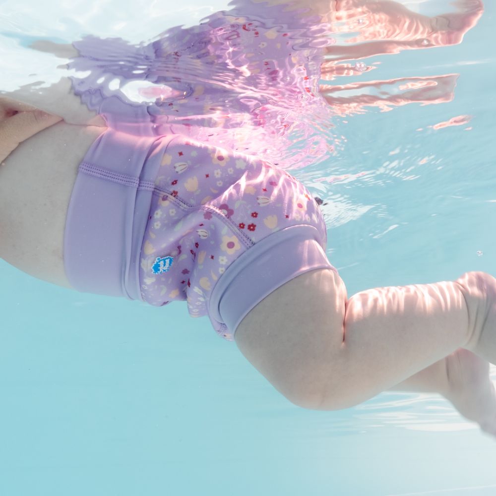 A baby shown swimming in a pool wearing a lilac swimming nappy by Splash About 