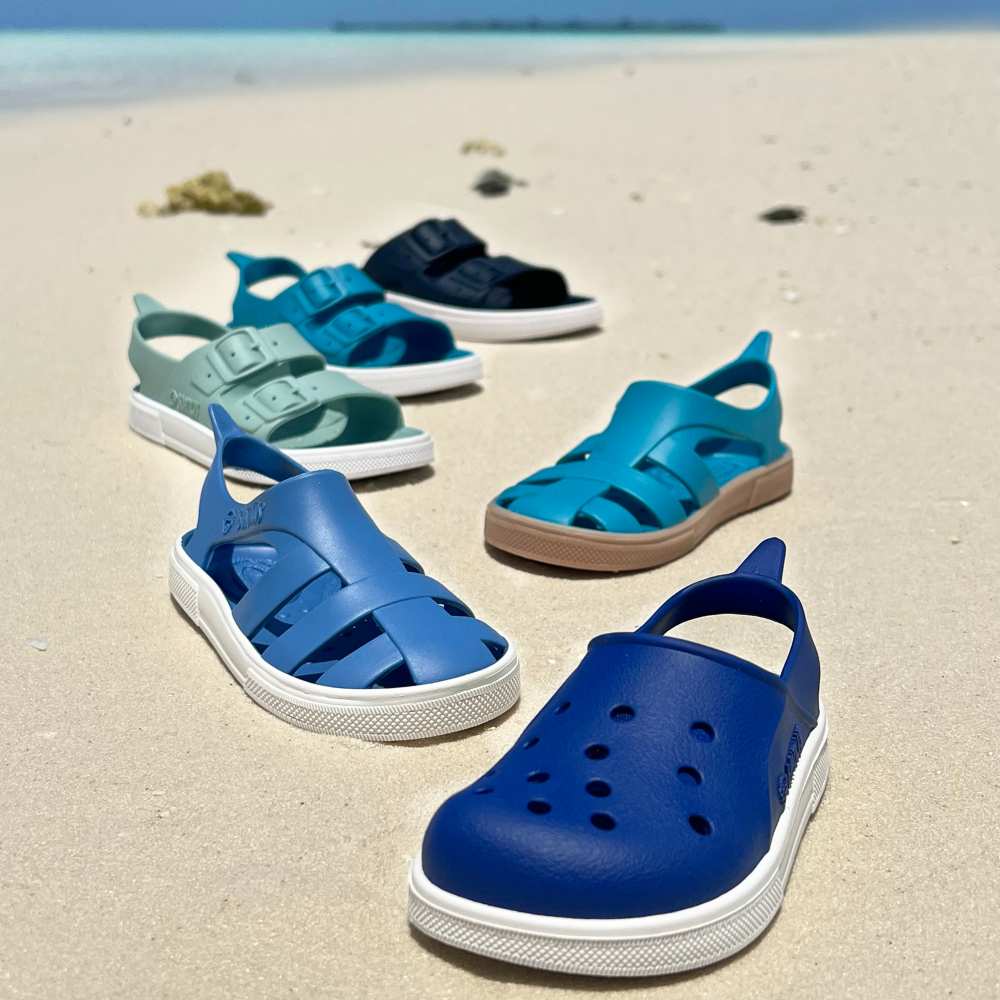 Children's summer sandals in different shades of blue displayed on a beach
