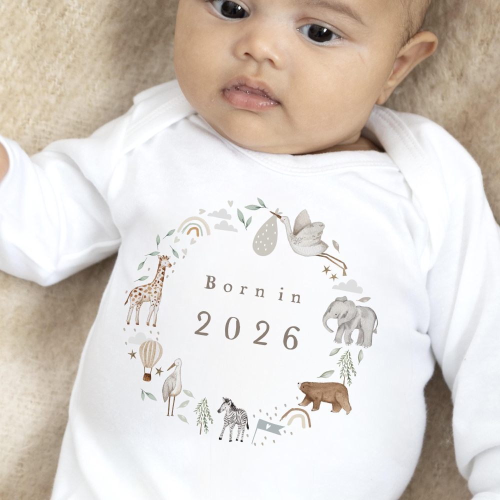 A baby wearing a white babygro with 'Born in 2026' and a design of animals on the front