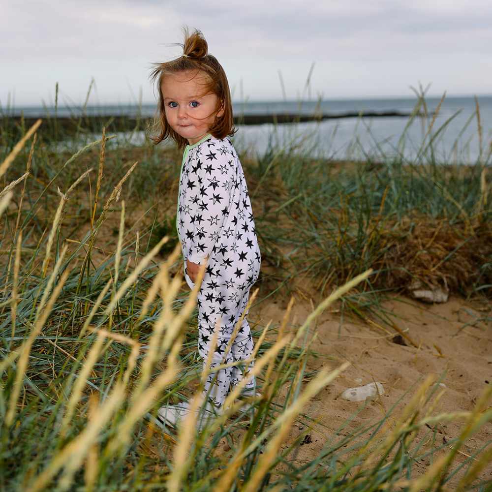 A young girl stood beside a lake wearing a white all in one with a black star print by Little'n