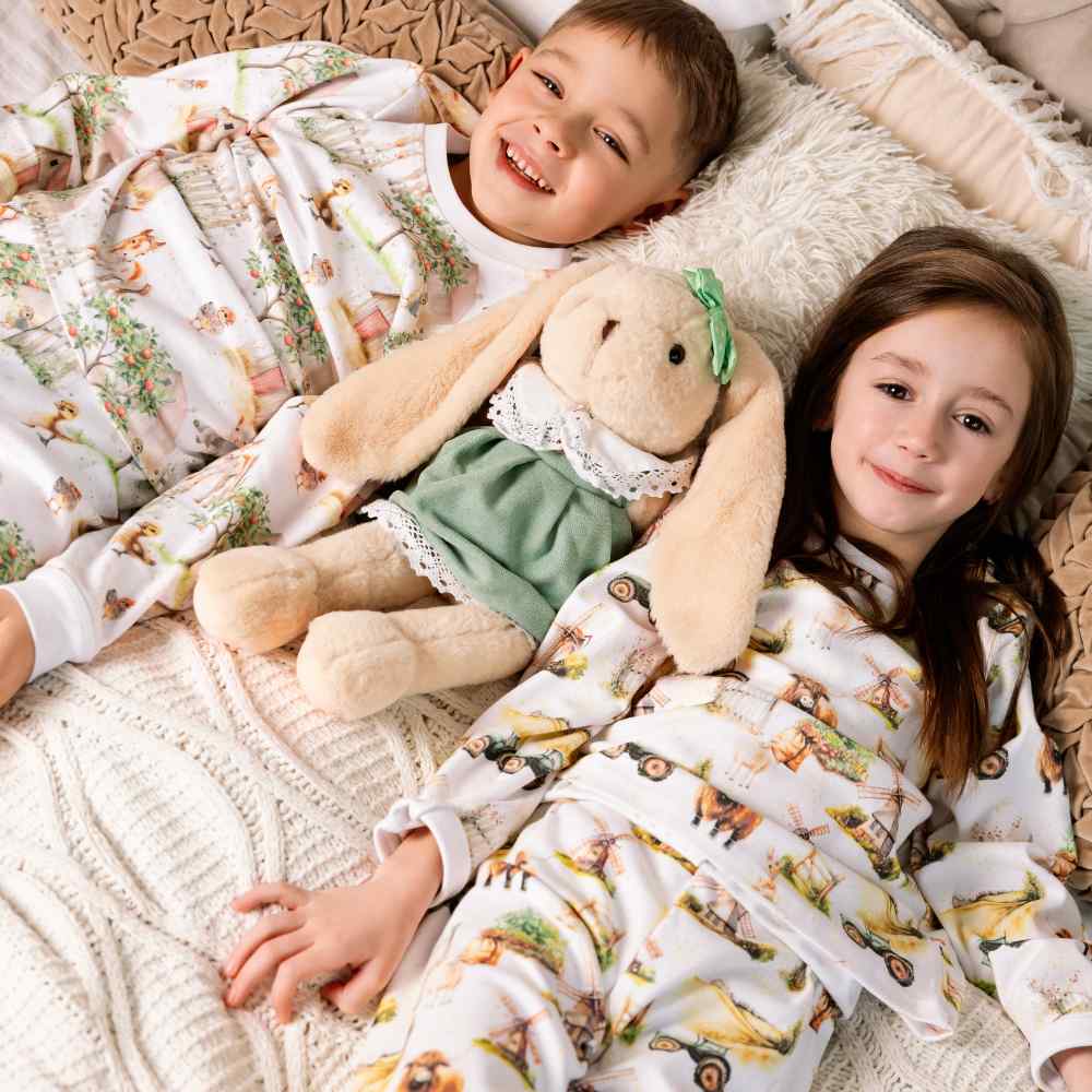 Two children lying on a bed wearing pyjamas with illustrative prints of animals