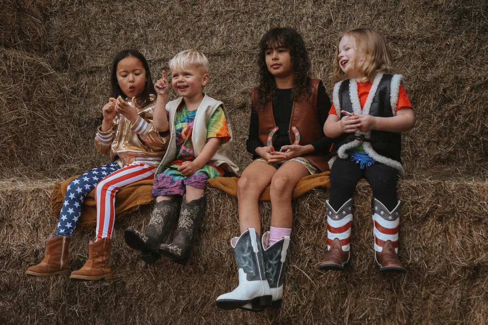 Children sat on a haystack wearing cowboy boots