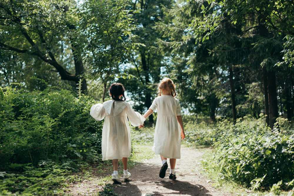 Two girls in white dresses walking through a wood