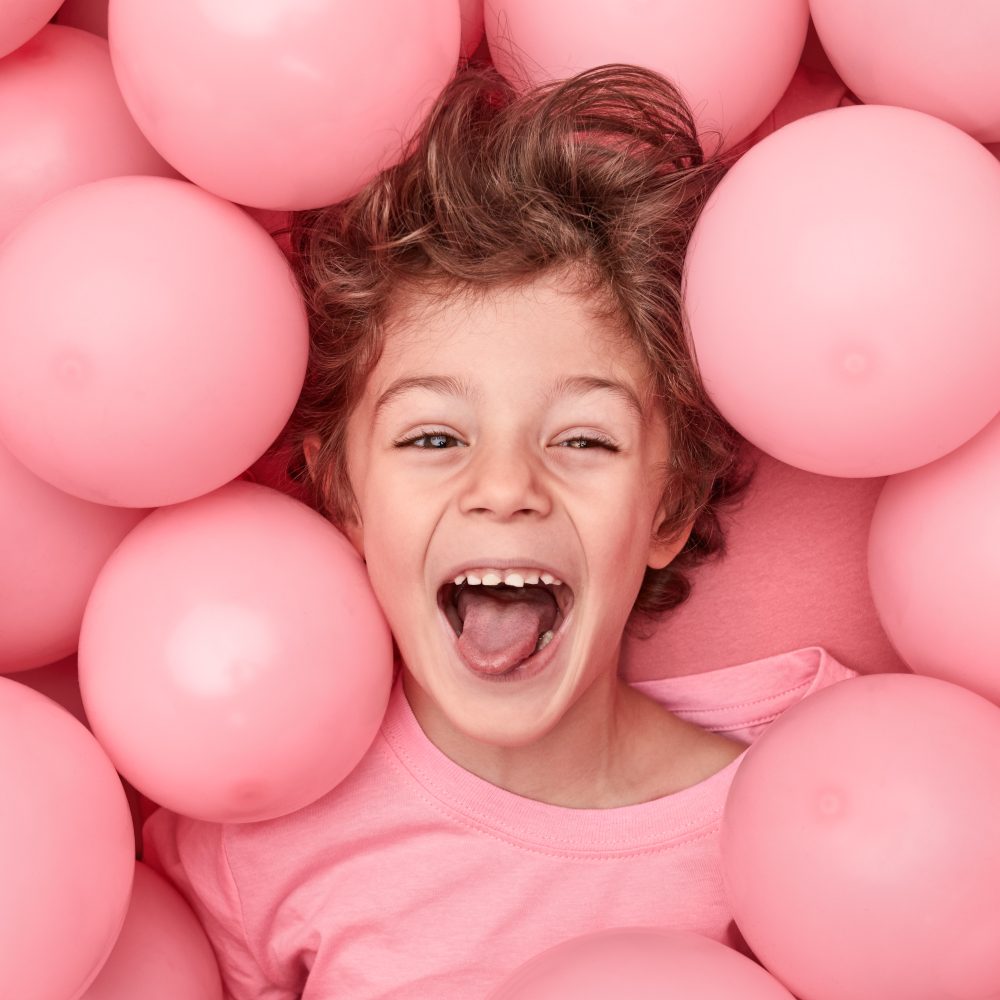 A smiling boy in a pink T-shirt surrounded by pink balloons