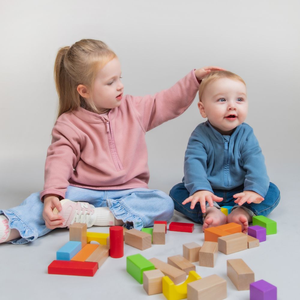 Two children sat on the floor playing with wooden blocks 