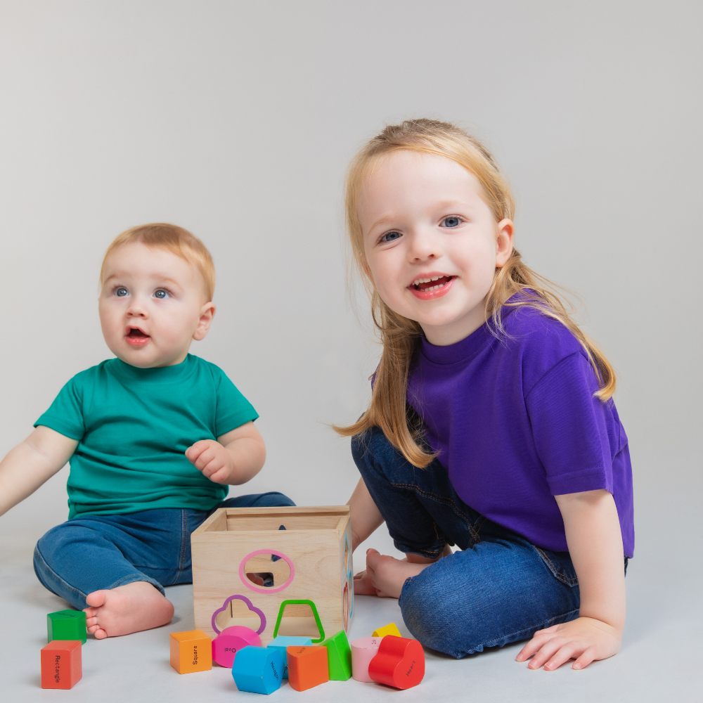 Two children sat on the floor playing with wooden blocks 