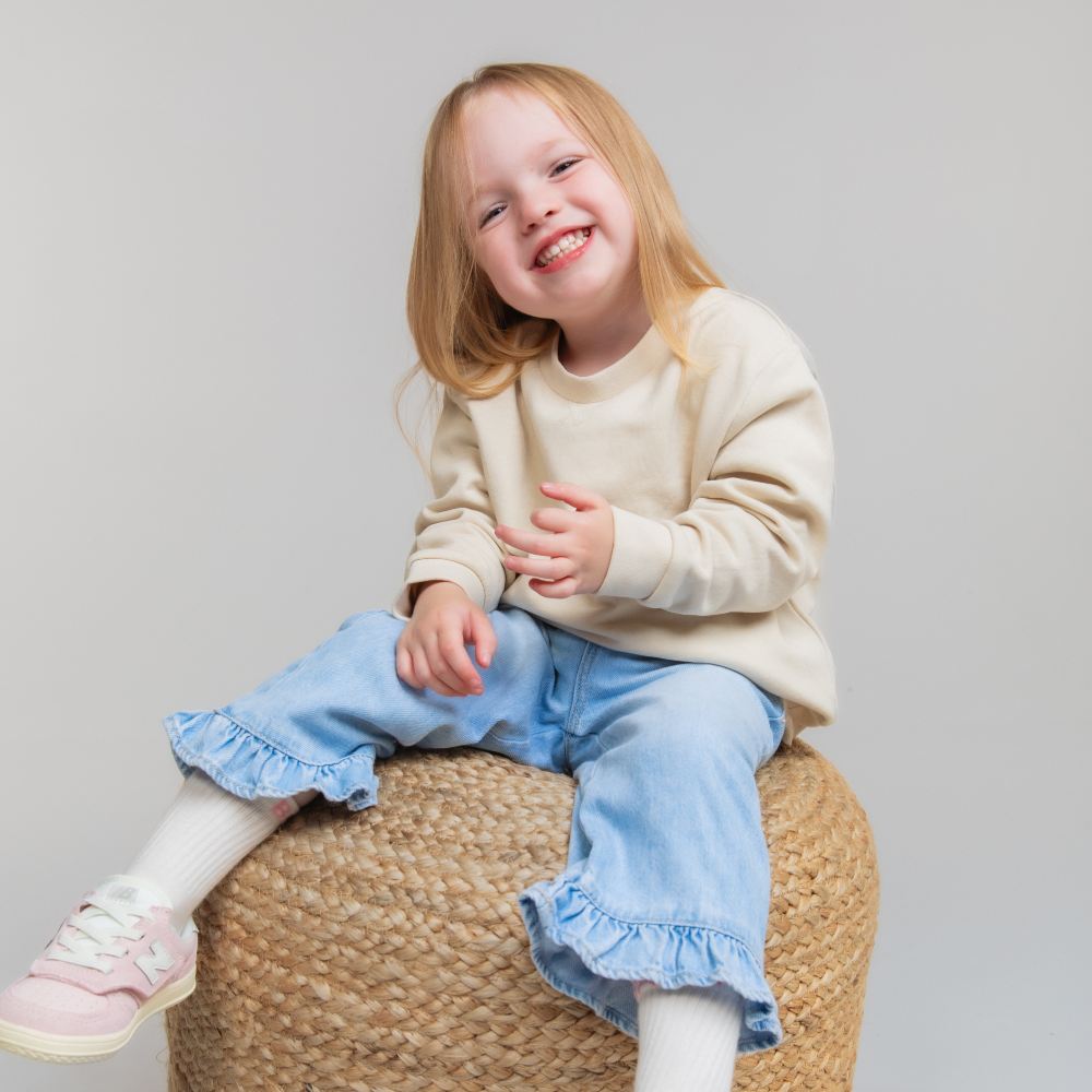 A smiling girl in a top and jeans sat on a rattan pouffe 