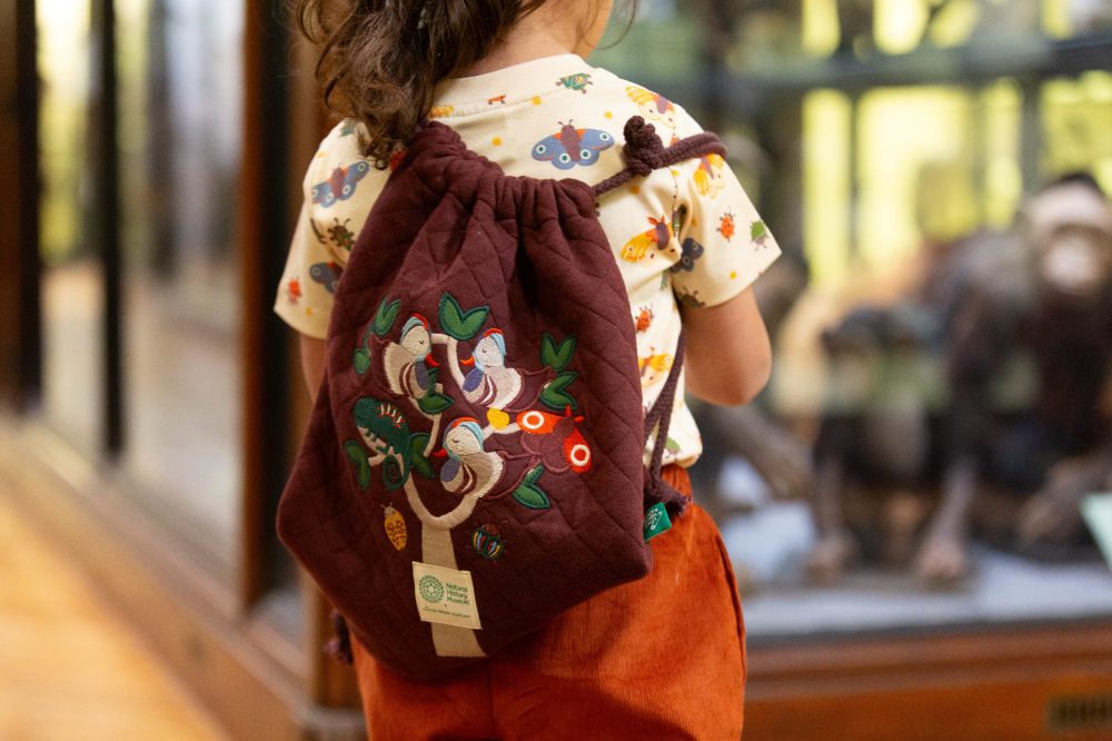 A girl stood beside a cabinet in the Natural History Museum with a drawstring bag on her back