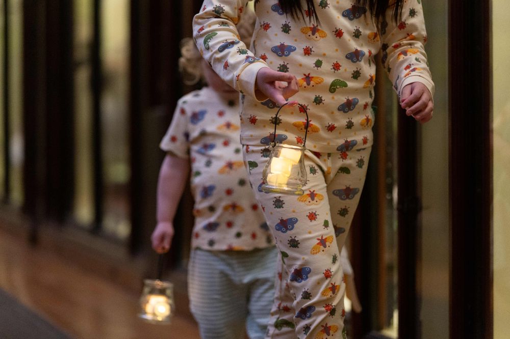 Children in pyjamas by Little Green Radicals holding lamps walking through the Natural History Museum 