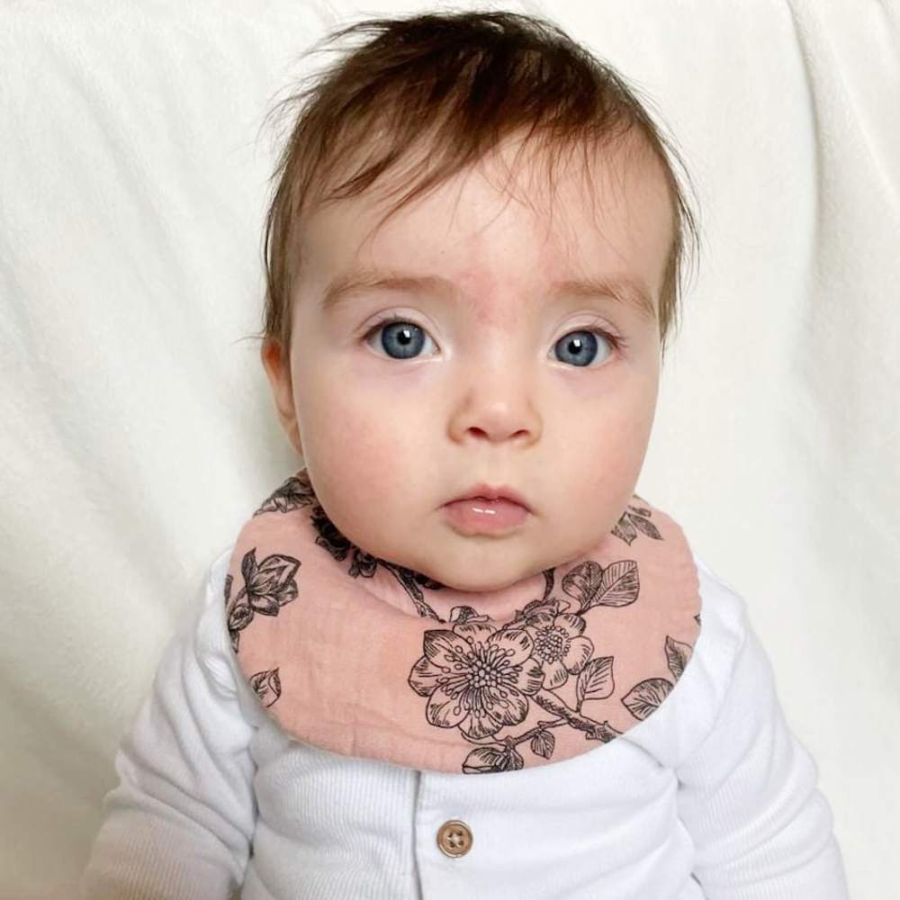 A baby in a white babygro and pink bib with a black floral pattern by Little Scandi Baby 