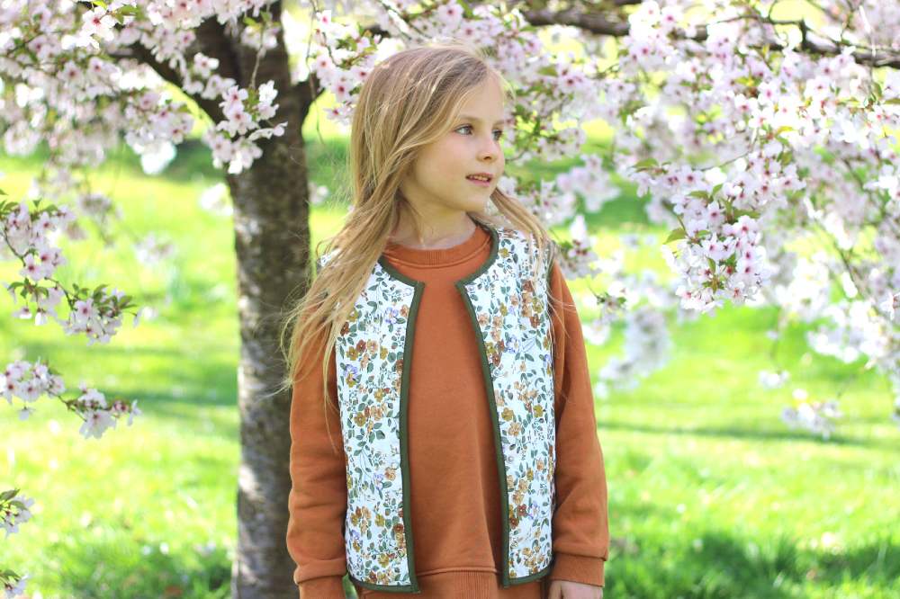A girl stood beneath a blossom tree wearing a floral vest by Little Scandi Baby