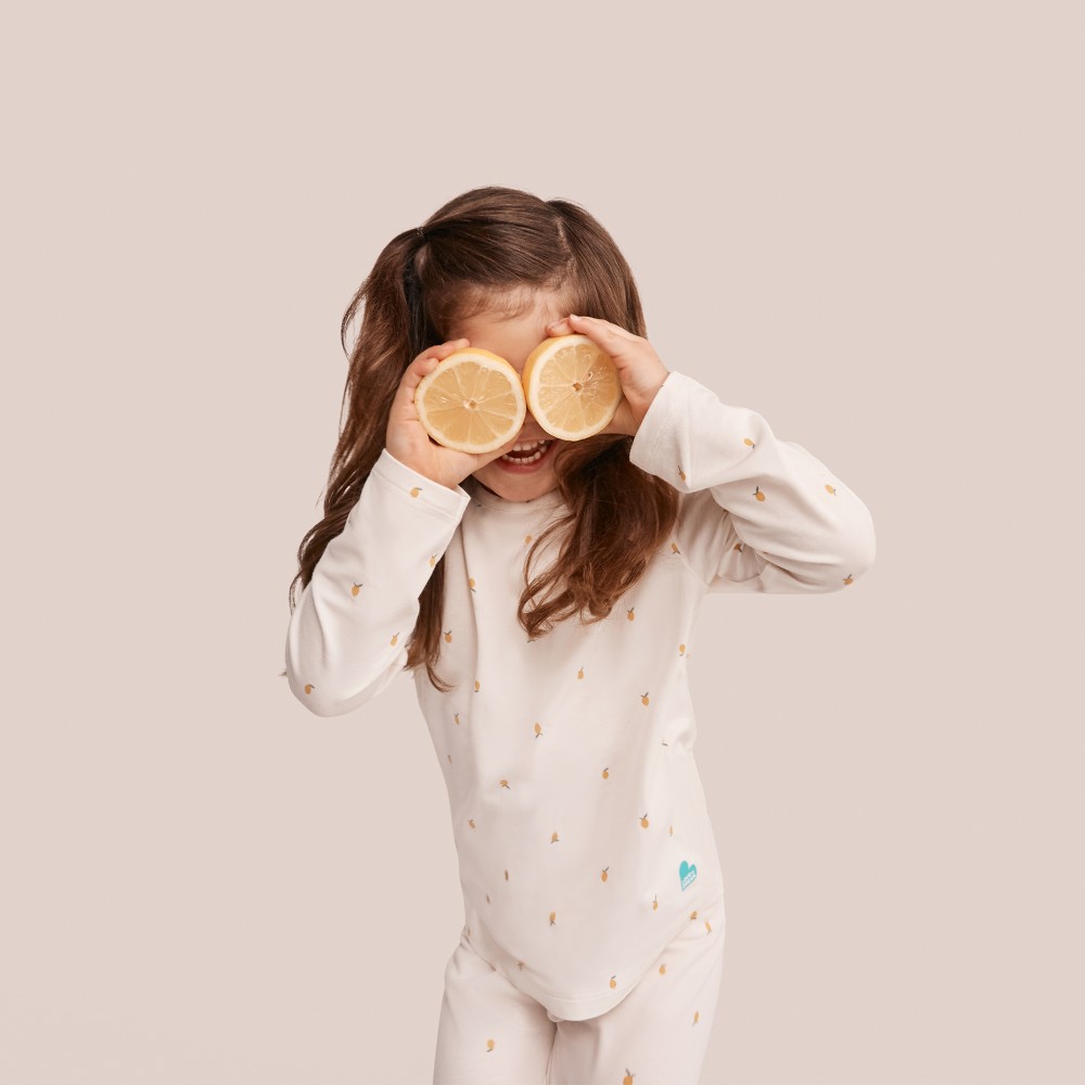 A child in lemon print pyjamas holding lemons up to her eyes 