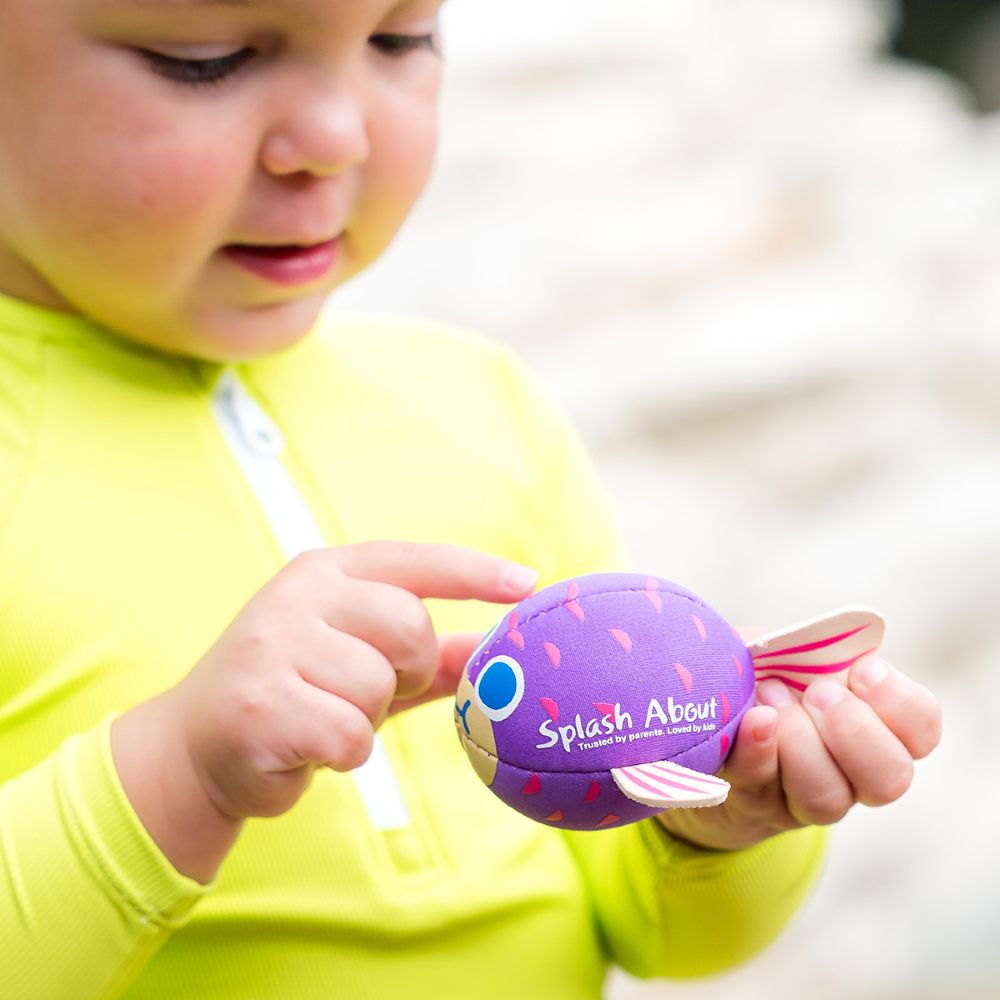 A young child holding a Splash About puffa fish bath toy