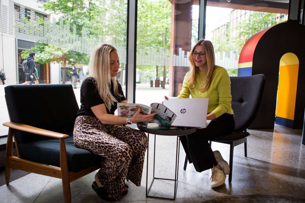 The founder of Threads Creatives sat at a desk with a laptop beside another woman