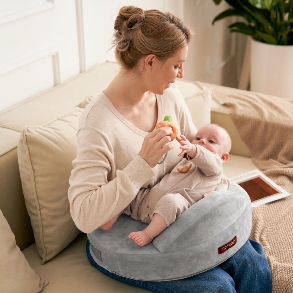 A woman sat on a coach with a baby laid on a Momcozy baby mat
