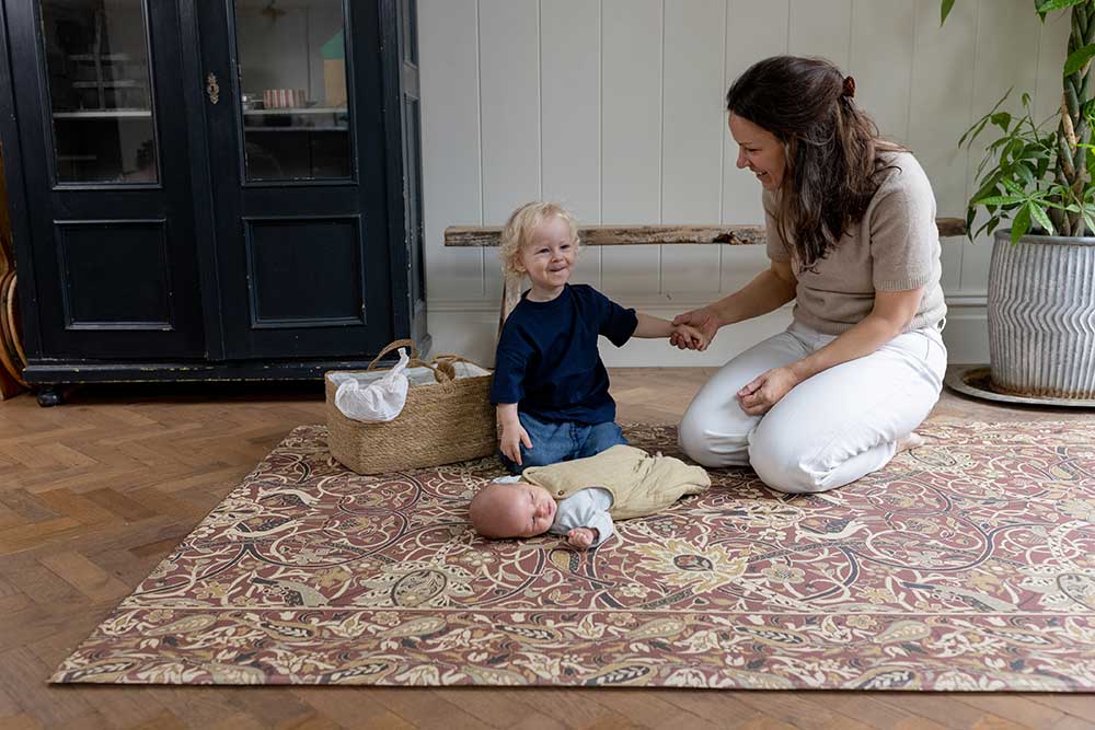 A mother sat on a playmat next to a baby and young child