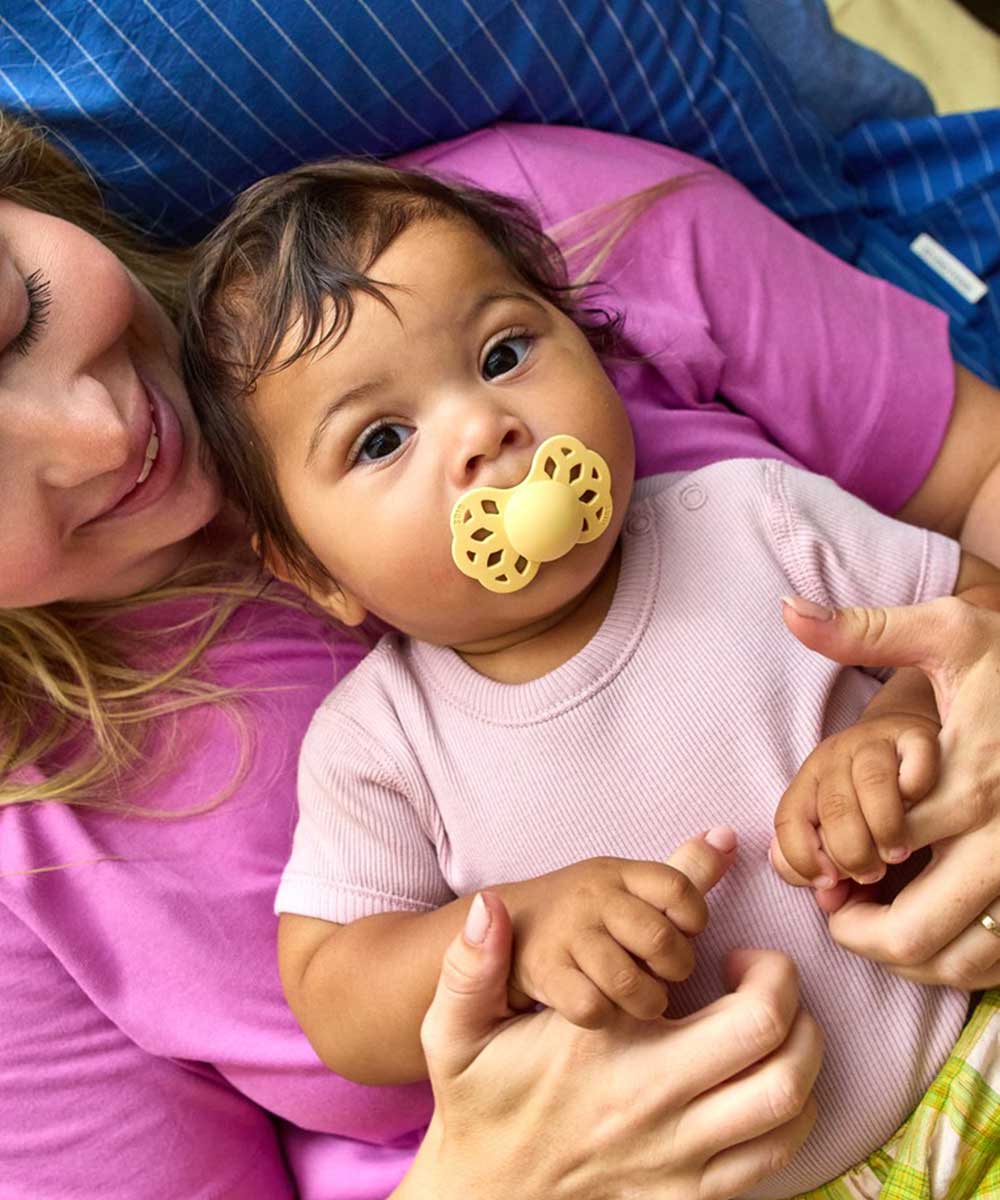 A mother laid down holding a baby with pacifier