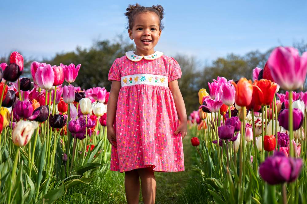 A girl stood in a tulip field wearing a pink summer dress by Frugi