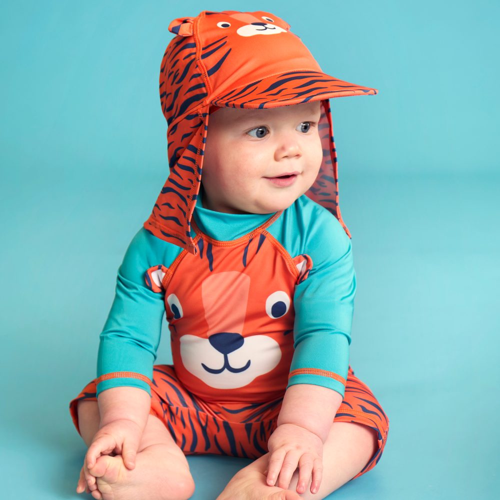 A sitting baby in a tiger design sun hat and swimsuit by Frugi 