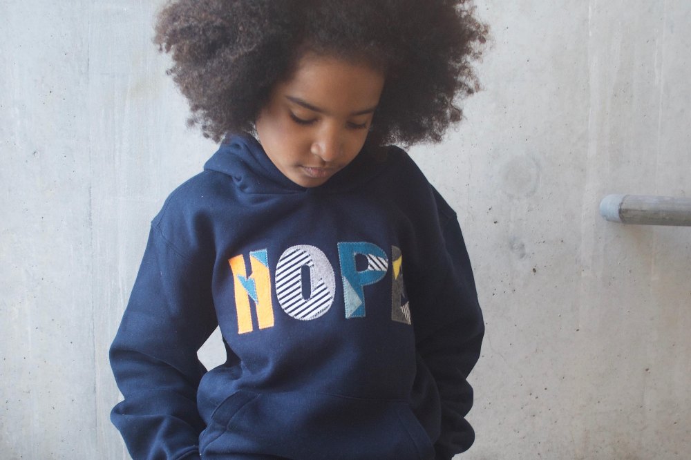 A child looking down wearing a sweater with 'Hope' on the front by Kin & Cloth